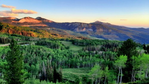 A scenic view of mountains and lush green forests under a colorful sunset sky.