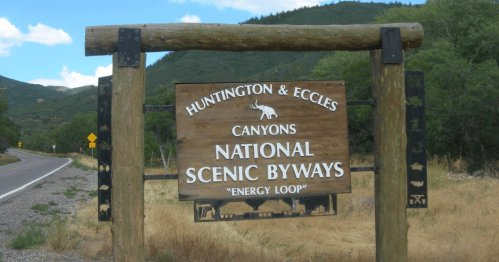 Sign for Huntington & Eccles Canyons National Scenic Byways, labeled "Energy Loop," surrounded by greenery and mountains.