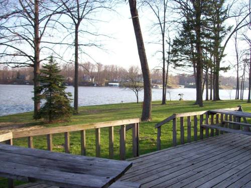 A serene lakeside view with trees, a grassy area, and a wooden deck overlooking the water.
