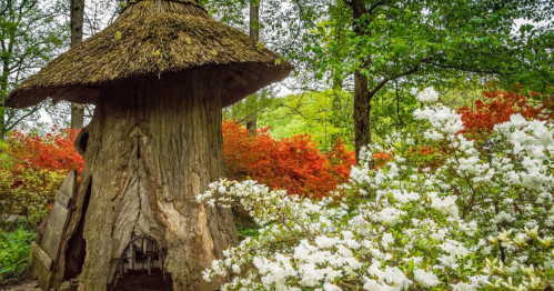 A whimsical treehouse with a thatched roof surrounded by vibrant flowers and lush greenery.