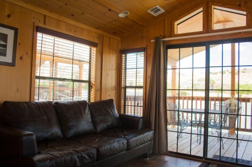 Cozy interior of a wooden cabin with a leather sofa and large windows overlooking a deck.