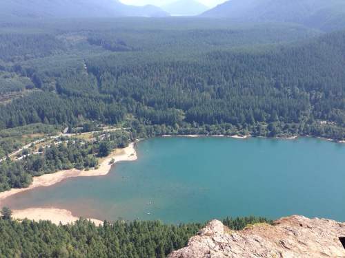 Aerial view of a serene lake surrounded by dense forests and mountains under a clear blue sky.