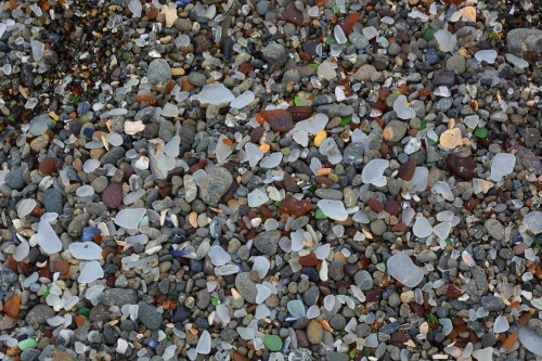 A close-up of a beach covered in a variety of colorful pebbles and sea glass, creating a textured mosaic.