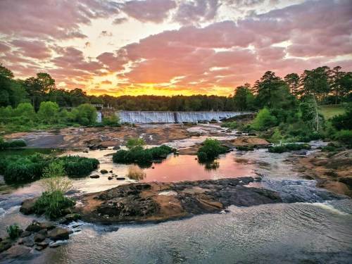 A serene river scene at sunset, with a dam in the background and lush greenery along the banks.