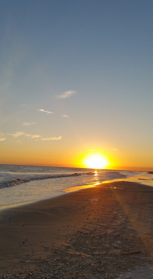 A serene beach at sunset, with golden hues reflecting on the water and gentle waves lapping at the shore.