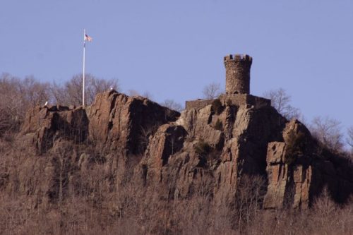 A stone tower atop a rocky hill, surrounded by bare trees, with an American flag flying nearby.