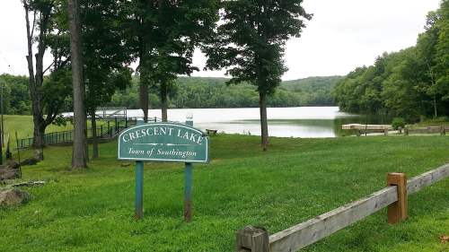 A serene view of Crescent Lake surrounded by greenery, with a sign in the foreground and calm water in the background.
