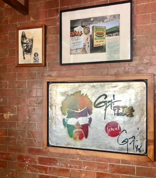 A wall featuring framed art and photographs, including a colorful portrait and vintage food-related documents.