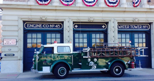 Vintage fire truck parked in front of Engine Co. 45 and Water Tower No. 1, decorated with patriotic bunting.