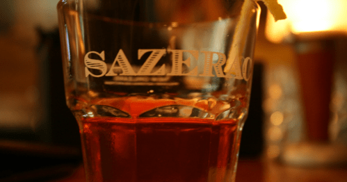 A close-up of a Sazerac cocktail in a glass, featuring a lemon twist garnish.