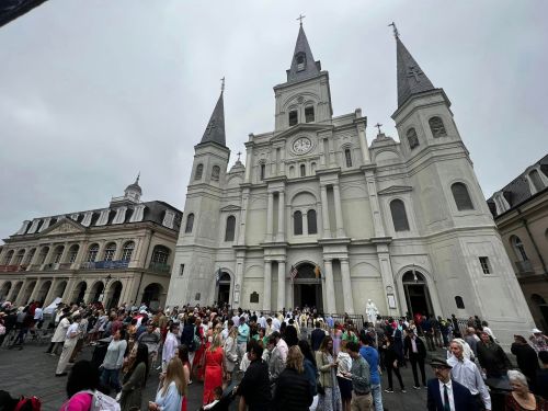 Crowd gathered outside a large, historic church with tall spires on a cloudy day in a bustling square.