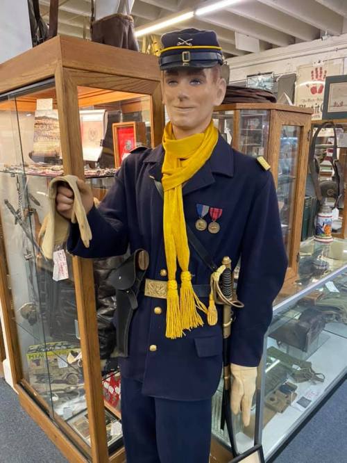 A mannequin dressed in a historical military uniform, holding gloves, with medals displayed on its chest.