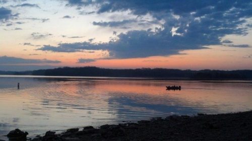 A serene lake at sunset, with a small boat on the water and colorful clouds reflecting in the calm surface.