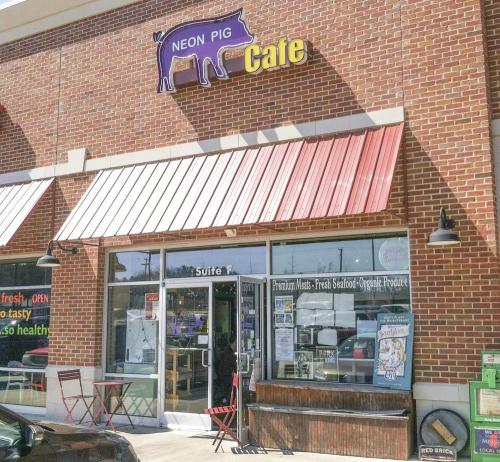 Exterior of Neon Pig Cafe, featuring a brick facade, red awning, and outdoor seating area.