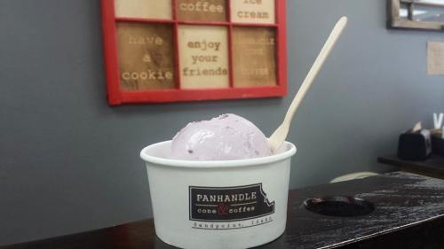 A cup of purple ice cream with a wooden spoon, placed on a counter in a cozy café setting.