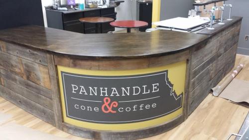 A wooden coffee counter with a sign reading "Panhandle Cone & Coffee" in a cozy café setting.