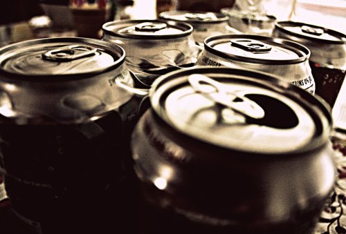 A close-up of several aluminum cans with pull tabs, slightly blurred, arranged closely together on a surface.