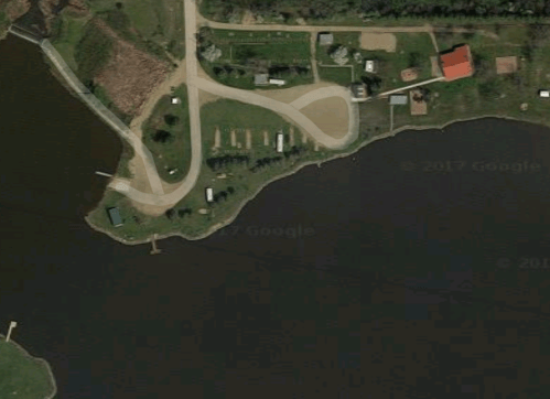 Aerial view of a lakeside area with roads, buildings, and green spaces along the water's edge.