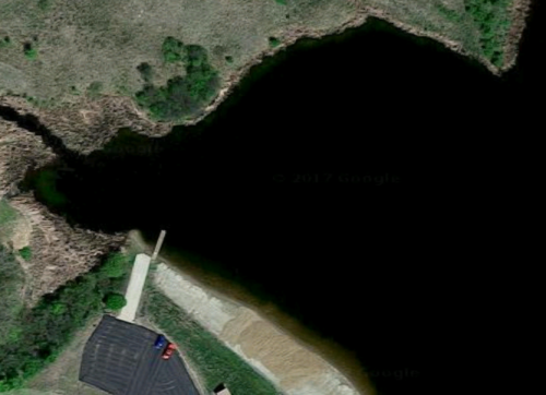 Aerial view of a dark lake surrounded by greenery and a small parking area near the shore.