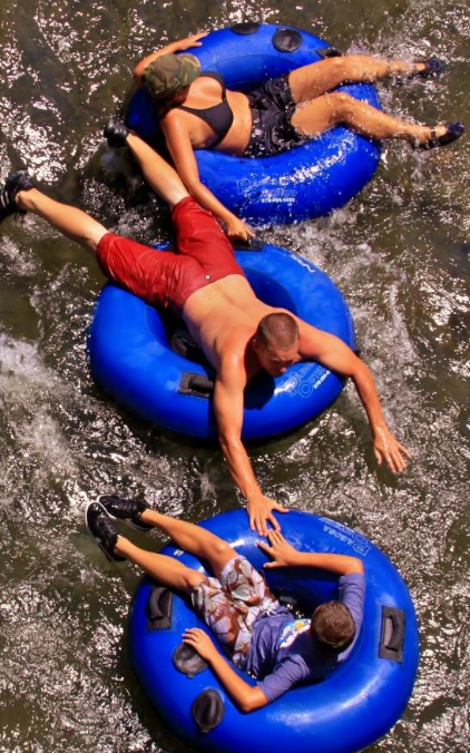 Three people float on blue inner tubes in a river, enjoying a sunny day. Water splashes around them.