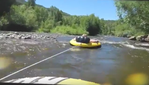 A yellow inflatable tube floats on a river, surrounded by lush greenery and rocky banks under a clear blue sky.