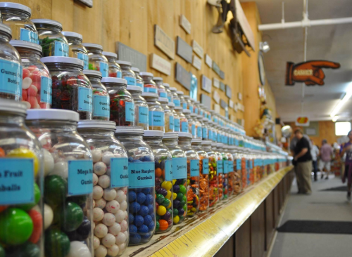 A colorful display of jars filled with various candies in a shop, with people browsing in the background.