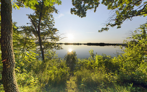 A serene lakeside view at sunrise, surrounded by lush greenery and reflecting water.