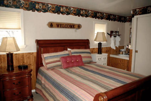 Cozy bedroom with a wooden bed, striped bedding, lamps, and a welcoming sign on the wall.