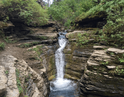 A serene waterfall cascades through rocky terrain, surrounded by lush greenery and trees.