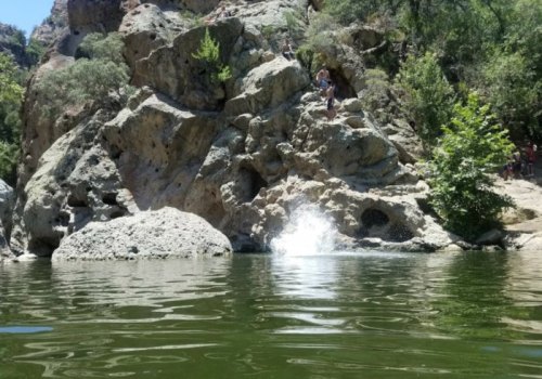 A rocky landscape with a clear greenish water pool, surrounded by trees and people enjoying the outdoors.