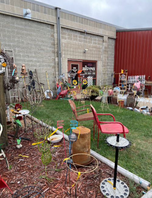 A quirky outdoor display featuring various vintage items, garden decor, and colorful chairs in a grassy area.