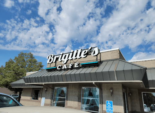 Sign for Brigitte's Cafe on a building with a blue sky and clouds in the background.