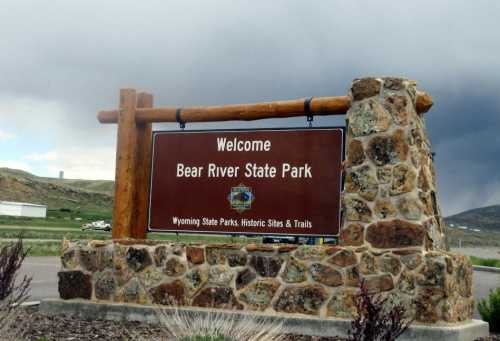 Welcome sign for Bear River State Park, featuring a wooden frame and stone base, set against a cloudy sky.