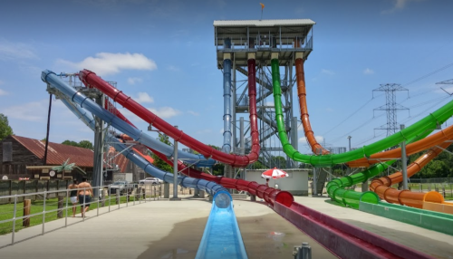 Colorful water slides at a water park, with a tall tower and a clear blue sky in the background.