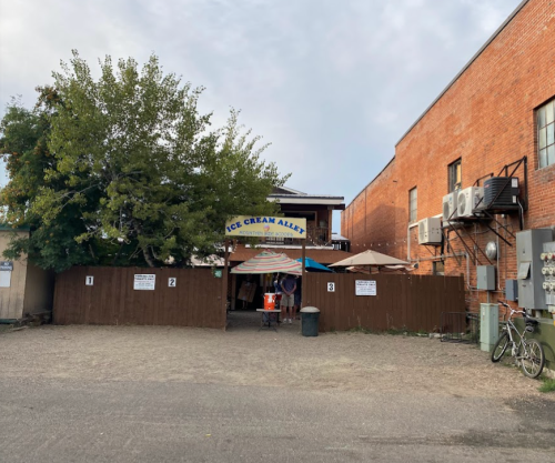 Entrance to "Ice Cream Alley," featuring outdoor seating, a tree, and a brick building in the background.