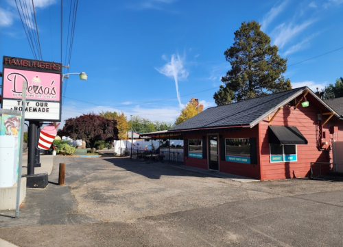 A small red hamburger restaurant with a sign, surrounded by trees and a clear blue sky.