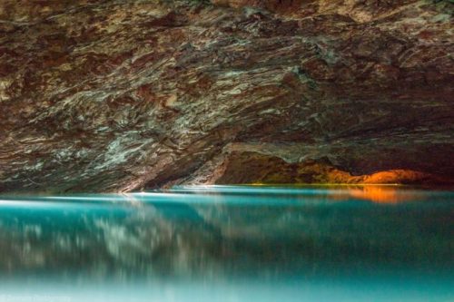 A serene underground cave with smooth rock formations and calm turquoise water reflecting the surroundings.