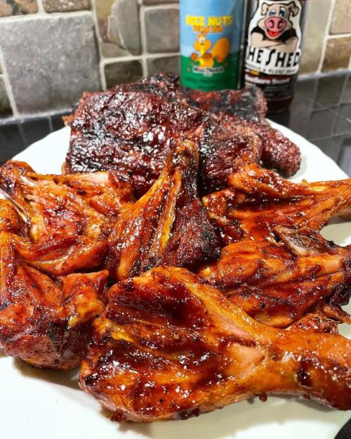 A platter of glazed chicken wings and smoked meat, with bottles of sauce in the background.