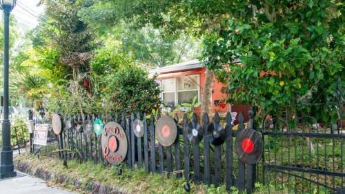 A colorful house surrounded by a black fence decorated with vinyl records and lush greenery.