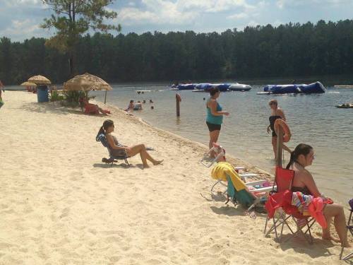 A sandy beach scene with people relaxing on chairs, swimming, and enjoying the water under a sunny sky.