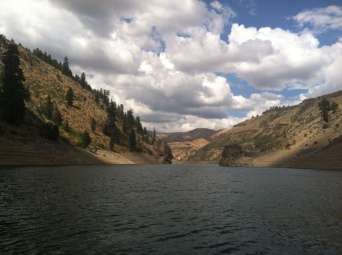 A serene lake surrounded by rocky hills and trees under a partly cloudy sky.