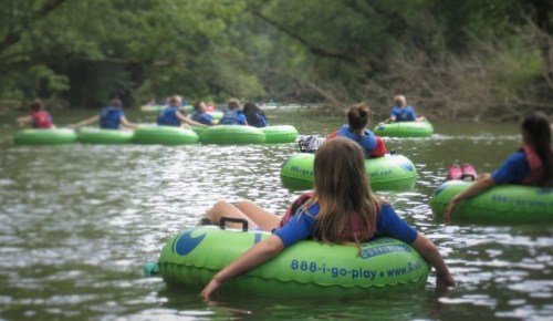 A group of people floating on green inner tubes down a calm river, surrounded by trees and nature.