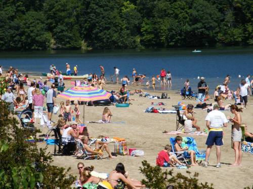 A crowded beach scene with people sunbathing, playing, and relaxing by the water on a sunny day.