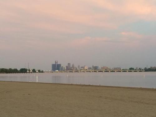 A serene view of a city skyline across a calm river at dusk, with a sandy beach in the foreground.