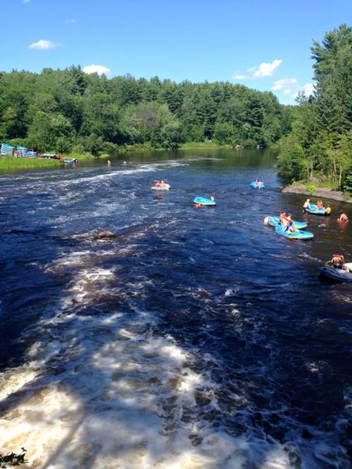 A scenic river with people kayaking and enjoying the water, surrounded by lush green trees and a clear blue sky.