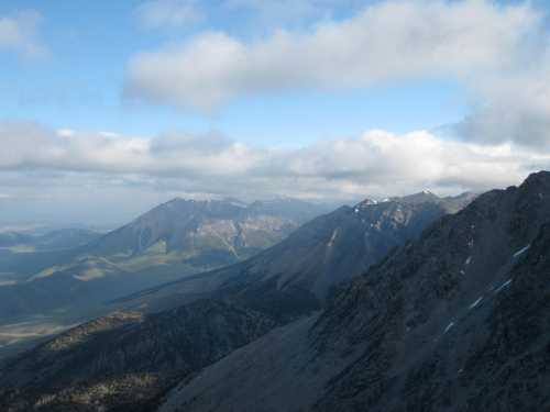 A panoramic view of rugged mountains under a partly cloudy sky, with green valleys stretching in the distance.