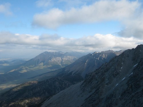A panoramic view of rugged mountains under a partly cloudy sky, with green valleys stretching in the distance.