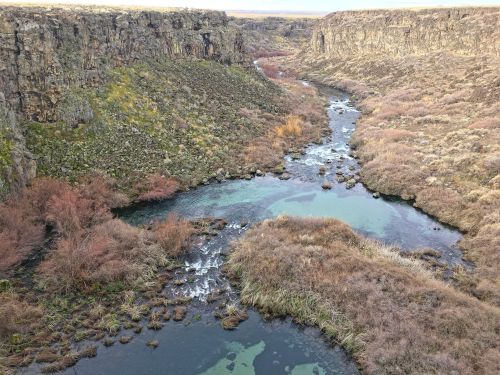 A winding river flows through a rocky canyon, surrounded by sparse vegetation and rugged cliffs.