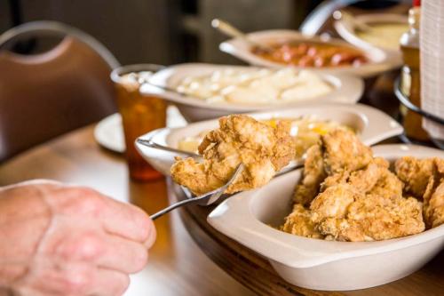 A hand holding a piece of fried chicken with various side dishes in the background on a dining table.