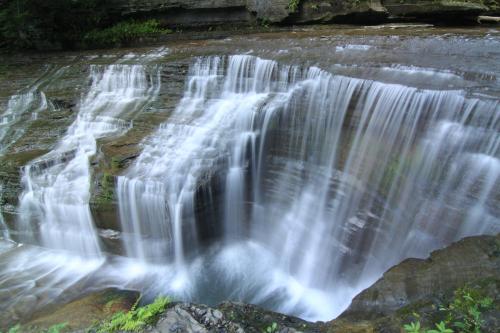 A serene waterfall cascading over rocky ledges, surrounded by lush greenery and smooth stones.